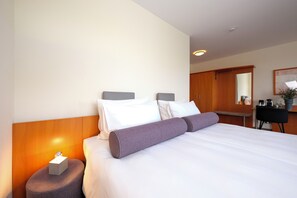 A hotel room with a bed, bedside table, lamp, and a desk with a chair.