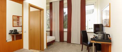 Une chambre d’hôtel avec un lit, un bureau avec un ordinateur, une chaise, un banc et une fenêtre avec des rideaux.
