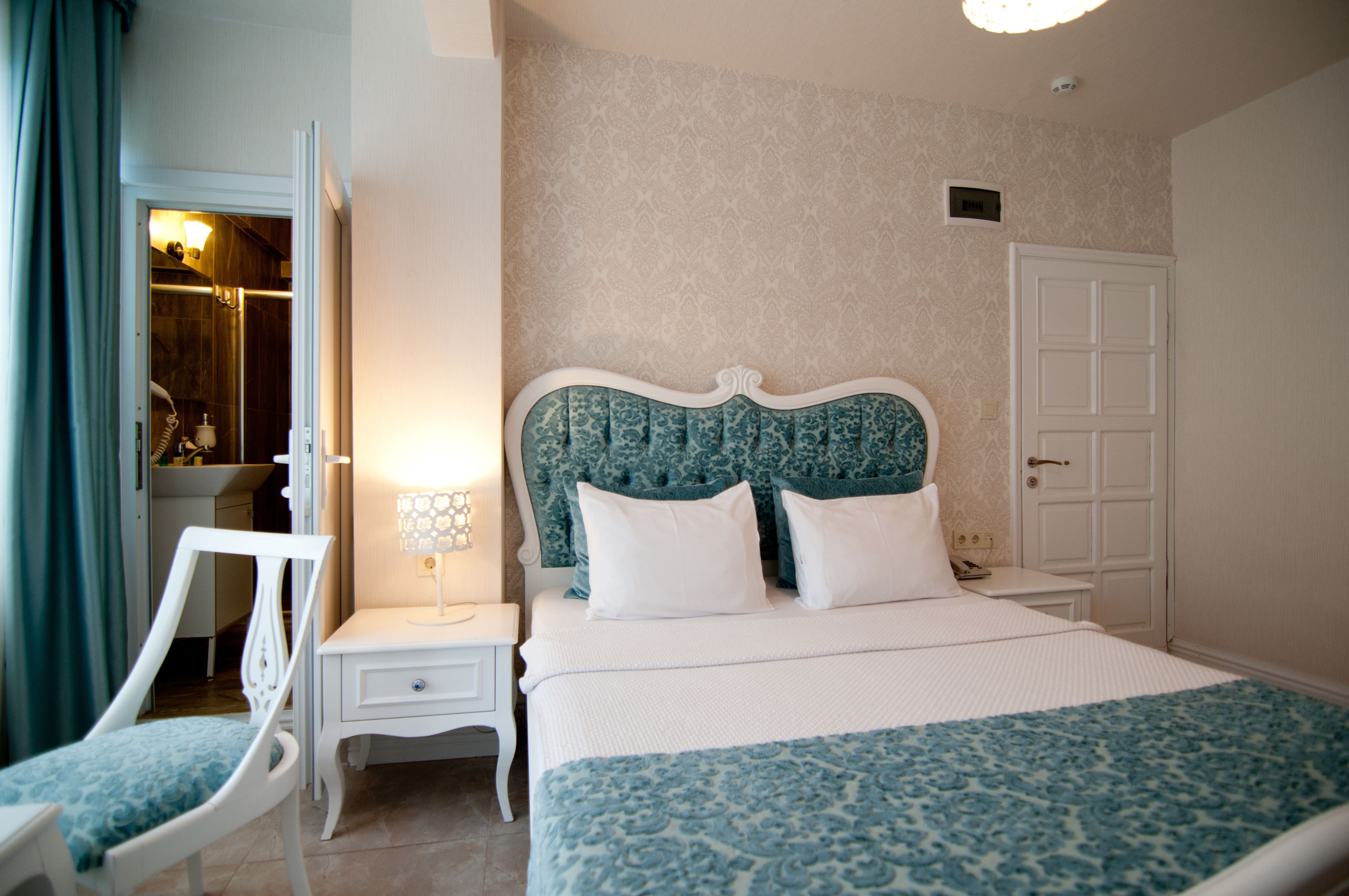 A neatly arranged bedroom with a bed, bedside table, chair, and a wardrobe.