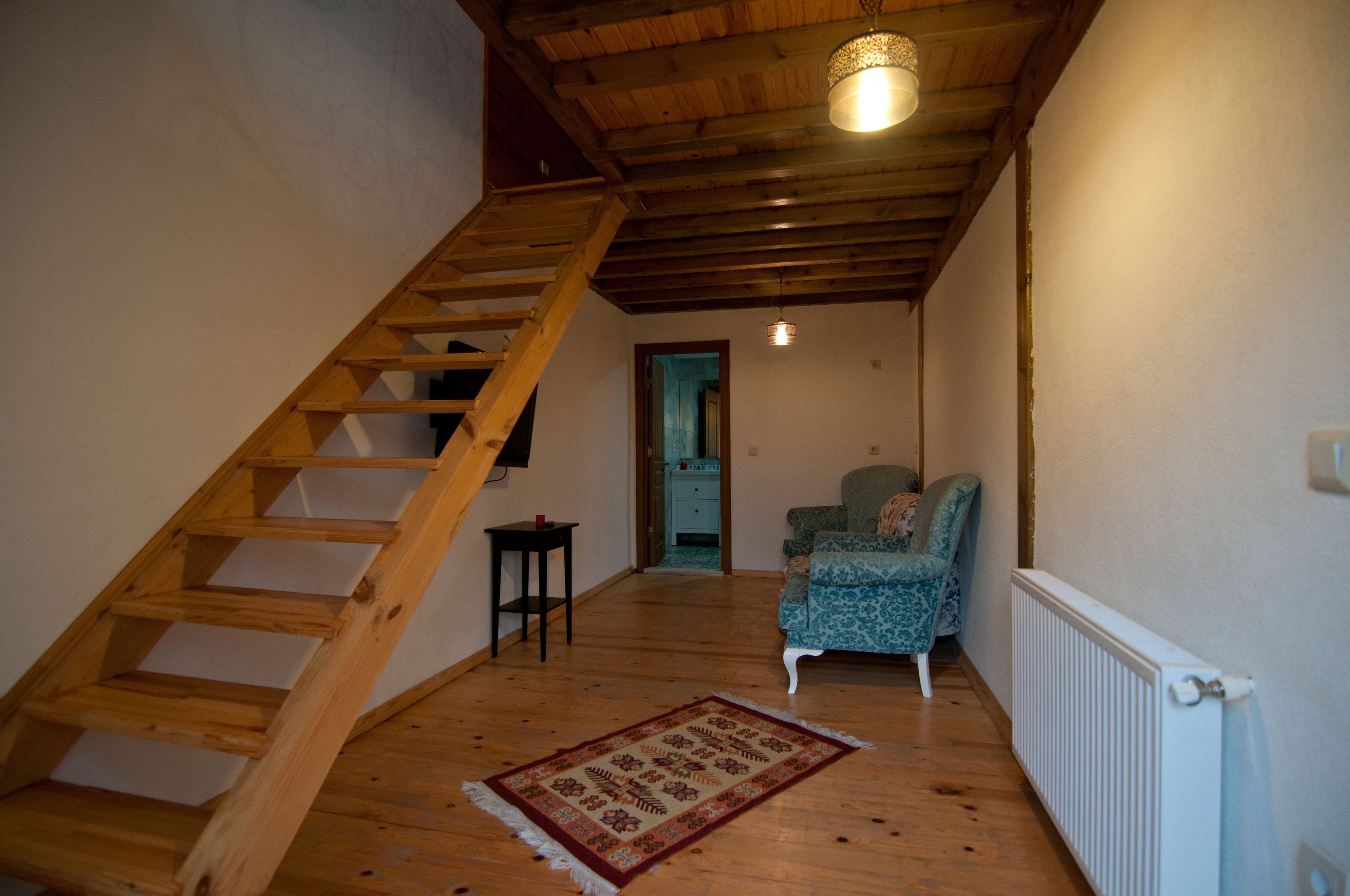 Una escalera de madera que conduce a un dormitorio con una alfombra estampada y una silla.