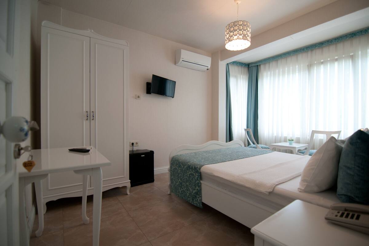 Une chambre à coucher comprenant un lit, une table de chevet, une armoire, un téléviseur et une fenêtre avec des rideaux.