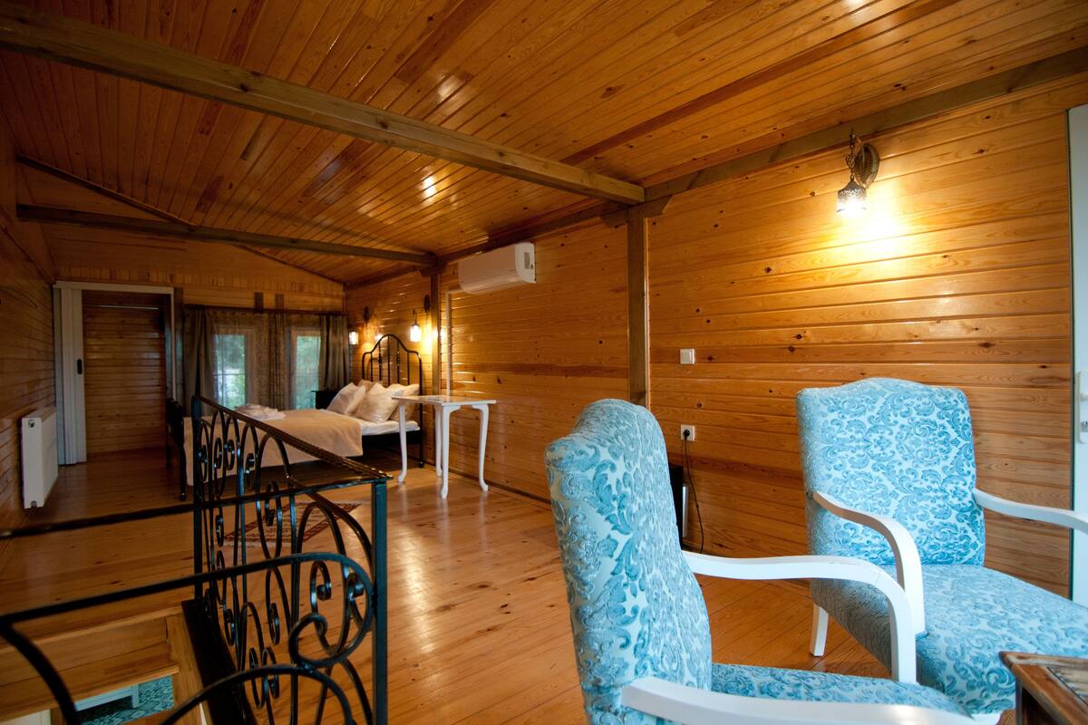 L’intérieur d’une cabane en bois, avec un lit, deux chaises, une table et un luminaire suspendu.