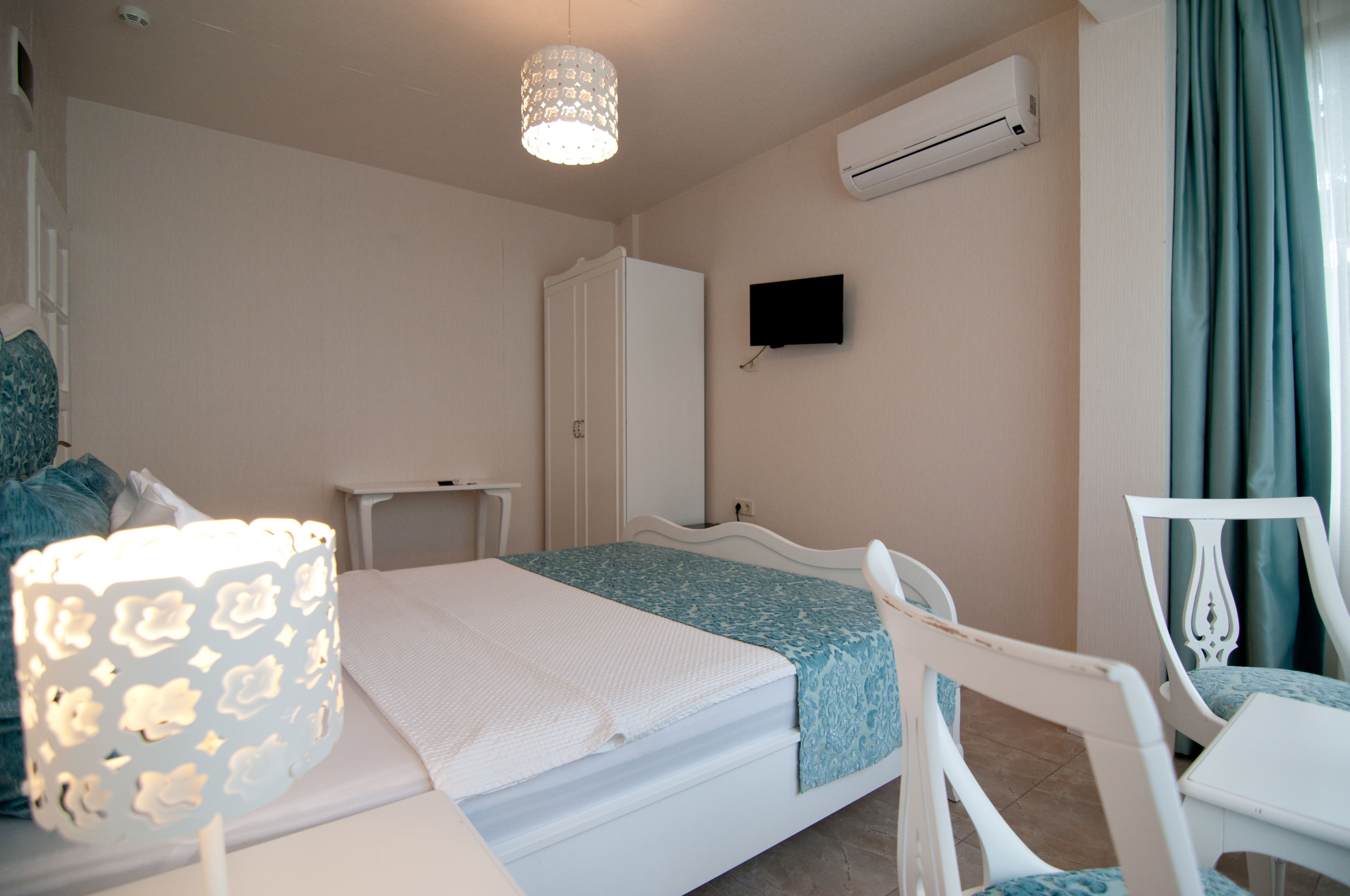 A bedroom with a bed, a bedside table, a lamp, a TV, and an air conditioning unit.
