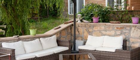 An outdoor seating area with wicker furniture, a glass table, and a stone wall.