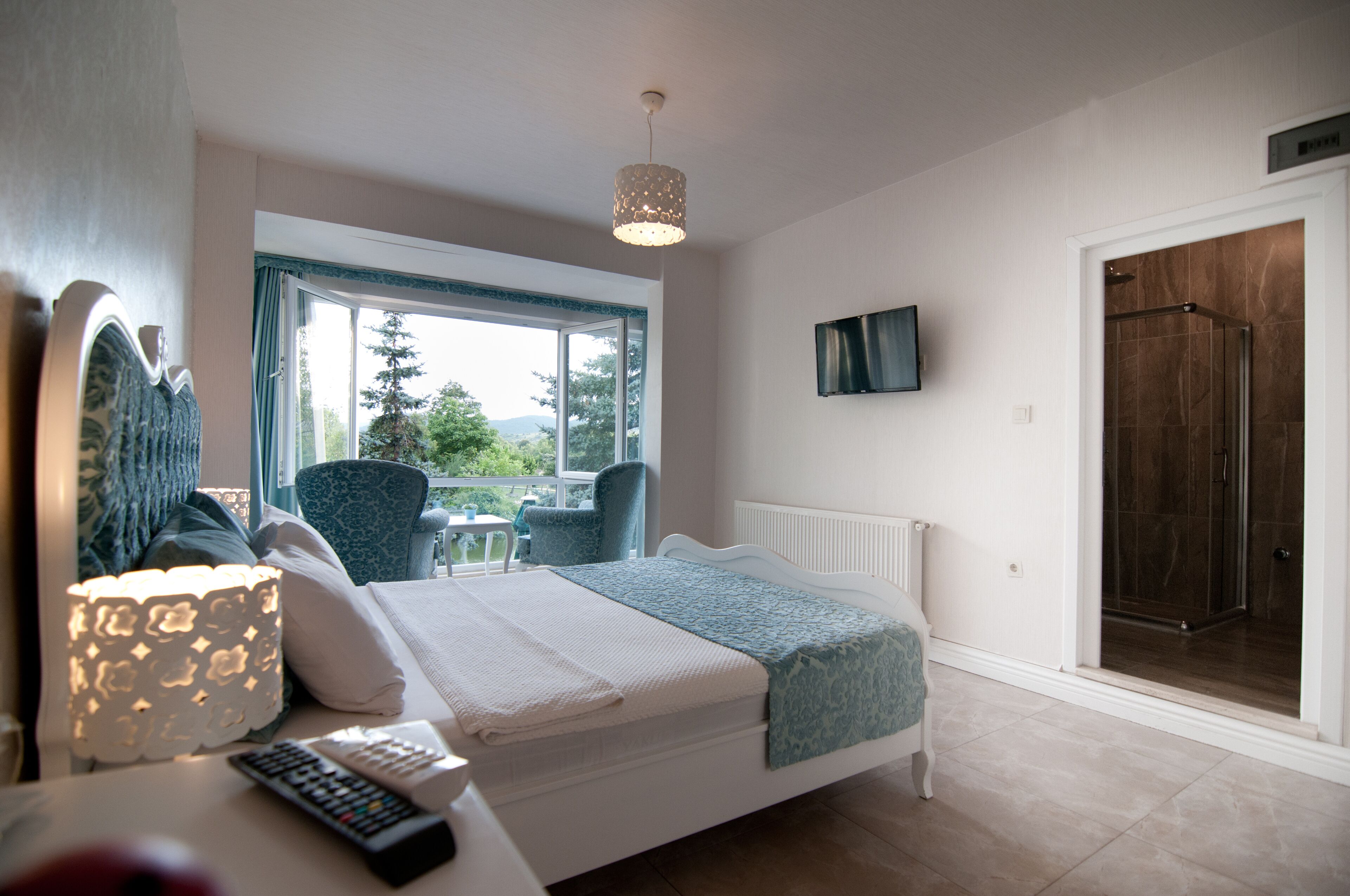 Un dormitorio con cama, una silla, una mesa con lámpara, televisión y zona de ducha.