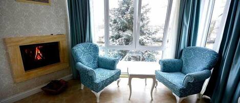 Un salón con dos sillones estampados, una chimenea de madera y vistas a un paisaje nevado a través de un ventanal grande.
