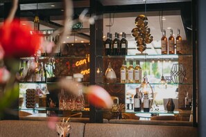 A bar area with shelves of bottles and glasses, a seating area with sofas, and a decorative hanging structure. - Hotel Schimmel (Woudenberg)