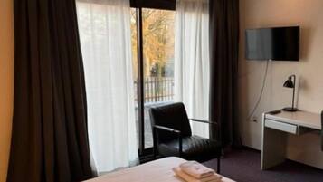 Ett hotellrum med två sängar, ett skrivbord, en stol, en TV och ett fönster med gardiner.