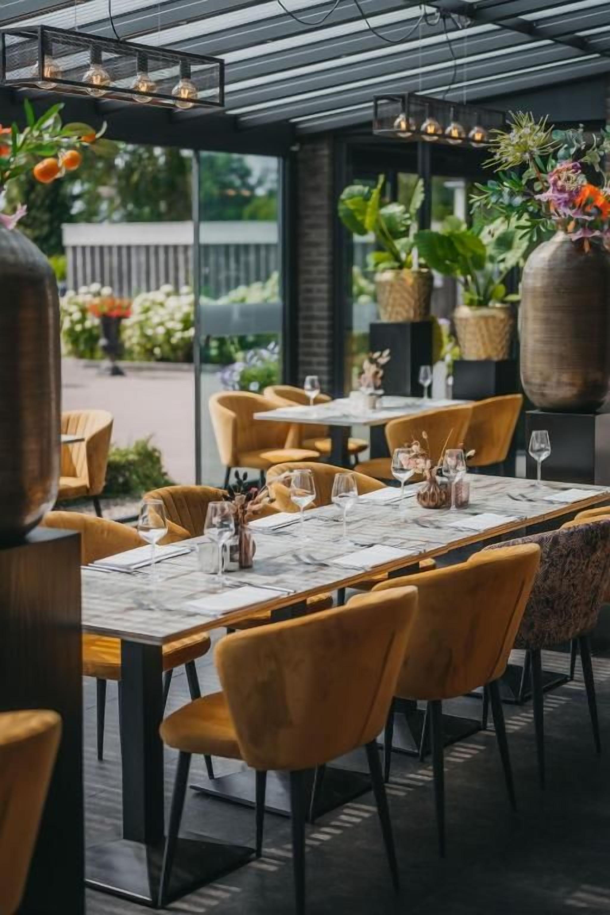 An outdoor dining area with tables and chairs, potted plants, and a pergola structure.