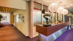 A reception area with a wooden counter, a sculpture, and decorative hanging lights. - Hotel Schimmel (Woudenberg)