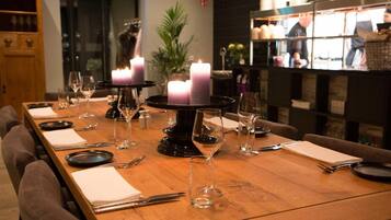 Una mesa de restaurante dispuesta con velas, copas de vino y platos, con un bar a la vista en el fondo.