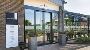 A modern building with large glass doors, a brick facade, and outdoor seating. - Hotel Schimmel (Woudenberg)