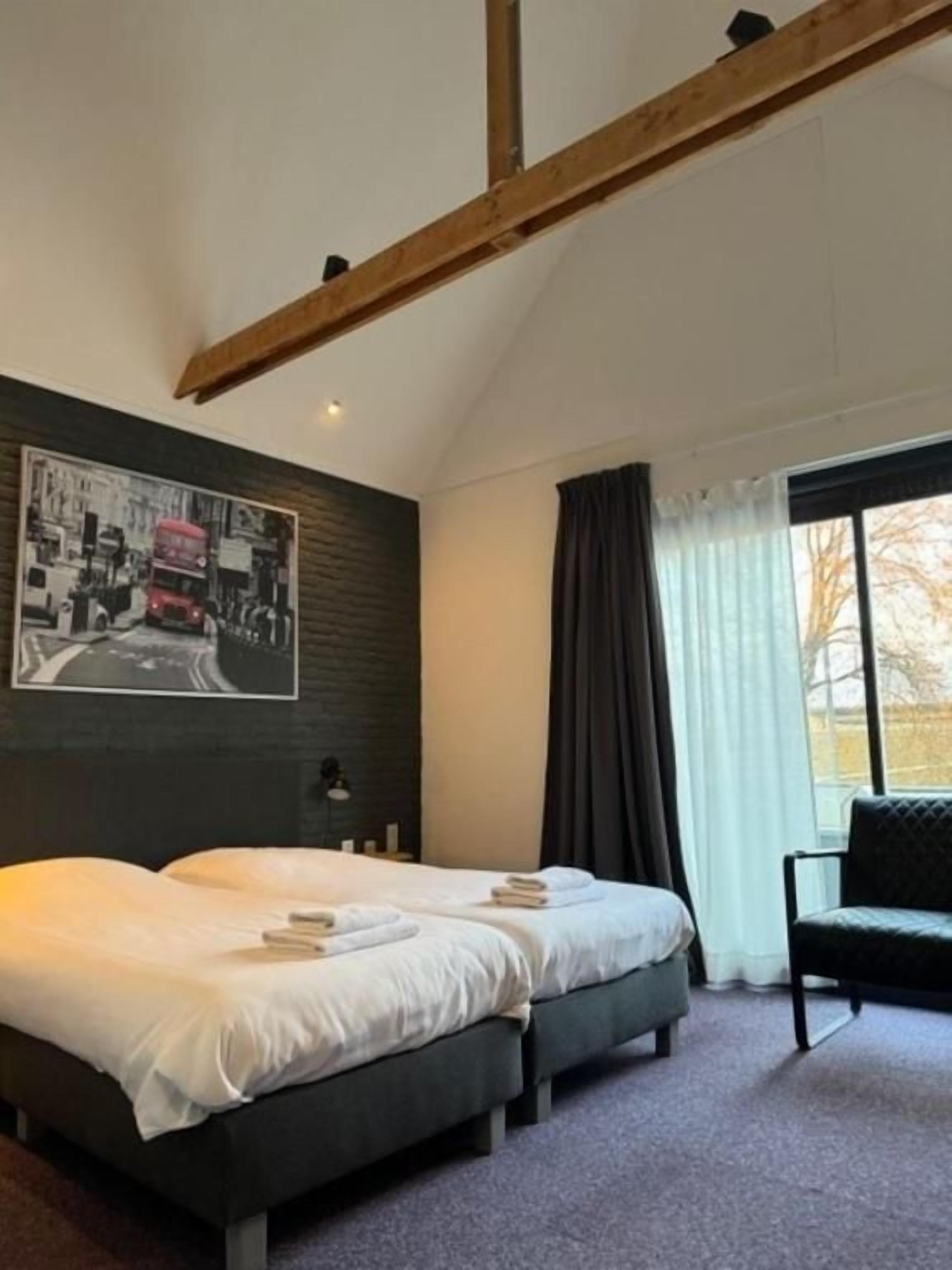 A bedroom with a bed, a chair, a window with curtains, and a wall-mounted picture.