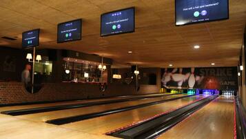 En bowlinghall med flera banor, skärmar i taket som visar spelgränssnittet och en tegelvägg med en neonreklamskylt.