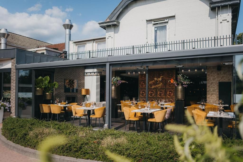 An outdoor dining area with yellow chairs and tables, a white building with a balcony, and a decorative wall with circular patterns.