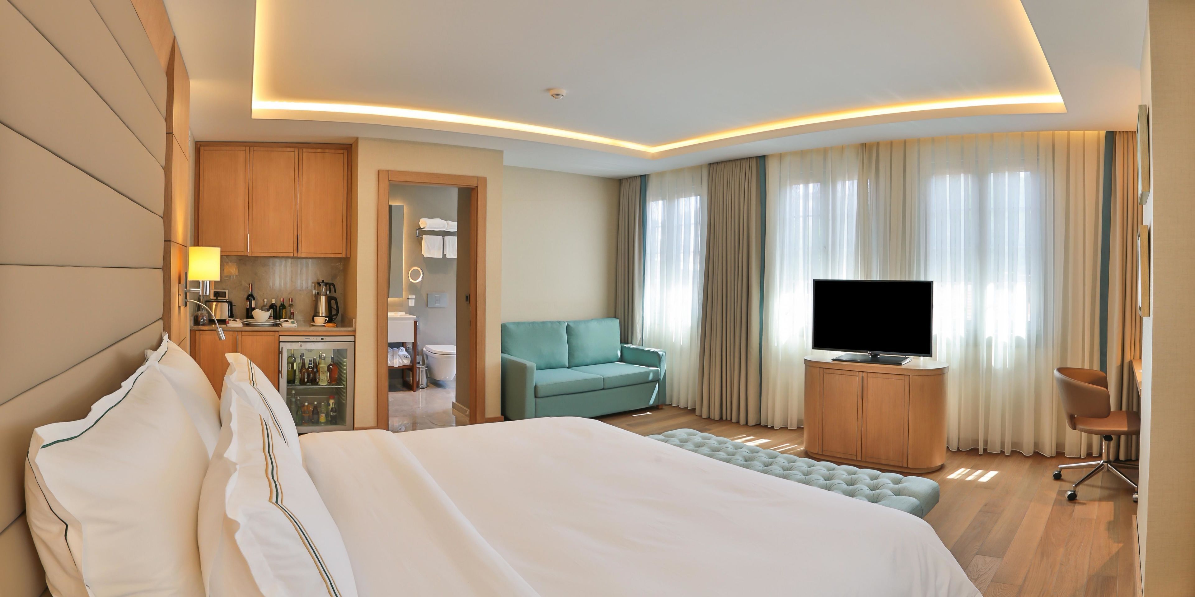 A hotel room with a bed, a television, a seating area, and a kitchenette.