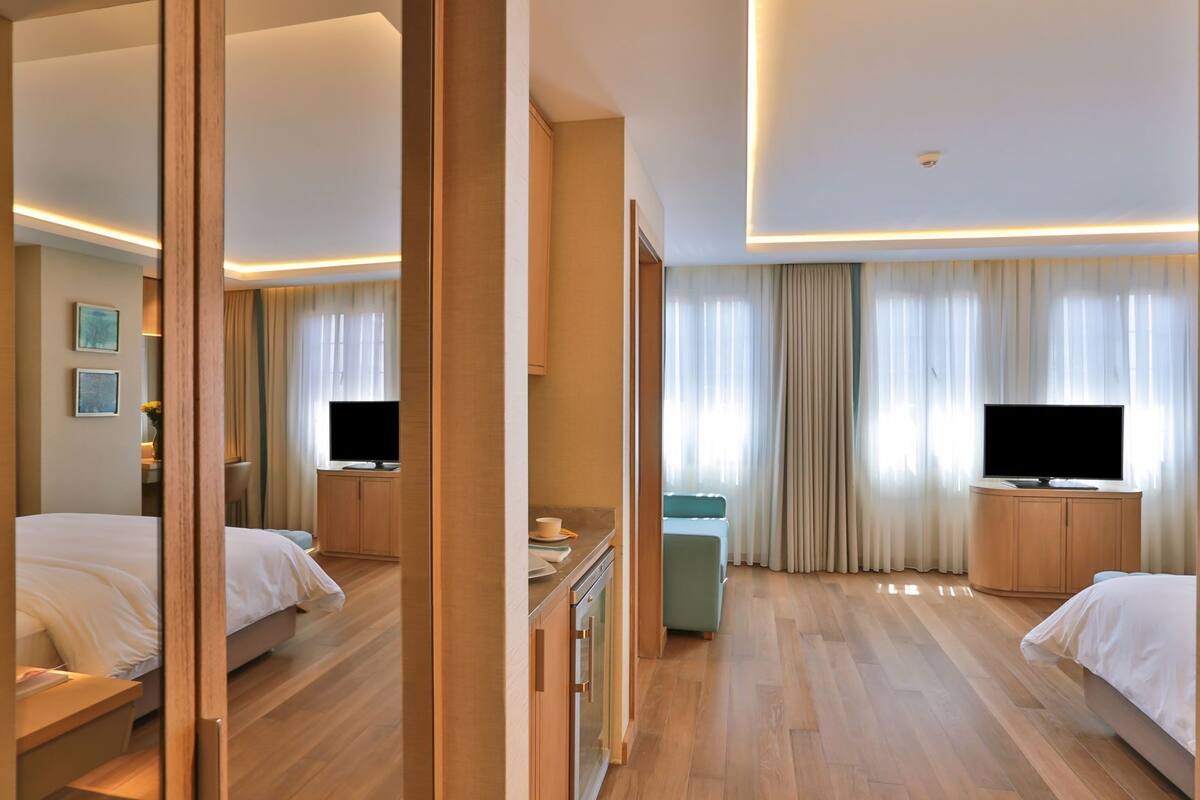A hotel room with two beds, a TV, a desk, and a mirror.