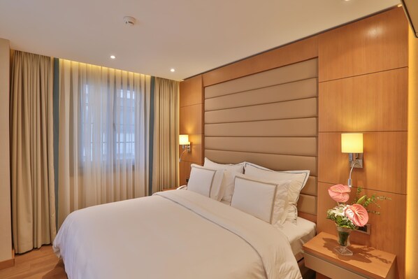 A hotel room with a large bed, wooden headboard, two bedside lamps, and a nightstand with a vase of flowers. - Ada Suites Nisantasi (Istanbul)