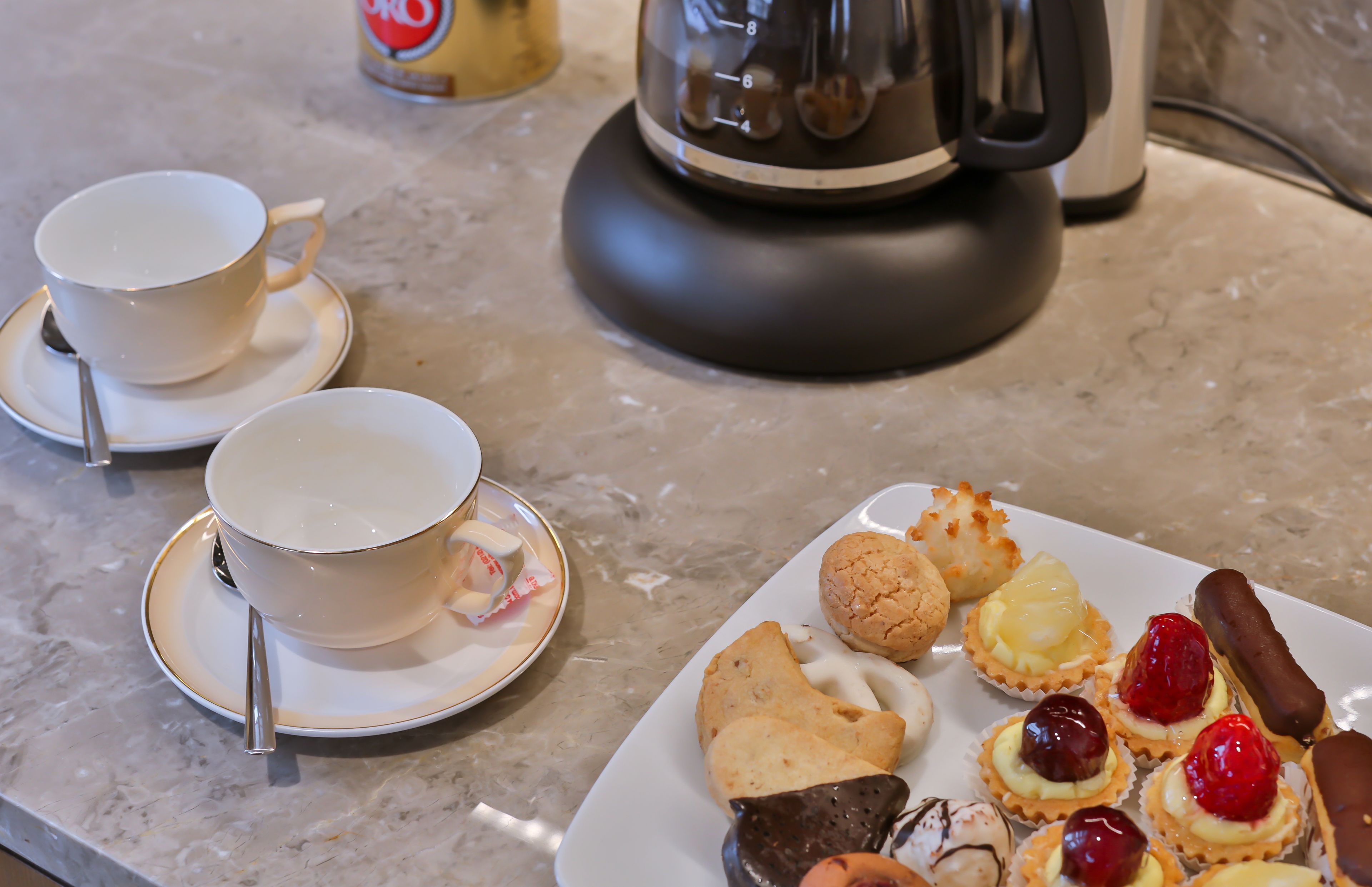 Une table avec deux tasses et leurs soucoupes, une assiette de pâtisseries et une machine à café.