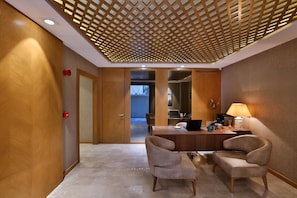 A hotel lobby with a wooden reception desk, two armchairs, a lamp, and a view into the dining area. - Ada Suites Nisantasi (Istanbul)