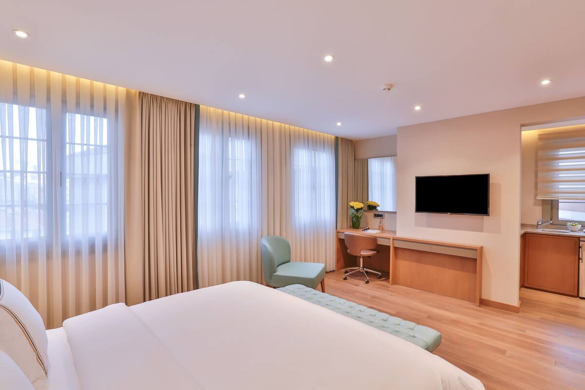 A modern hotel room with a large bed, a desk, a chair, a television, and a bathroom.