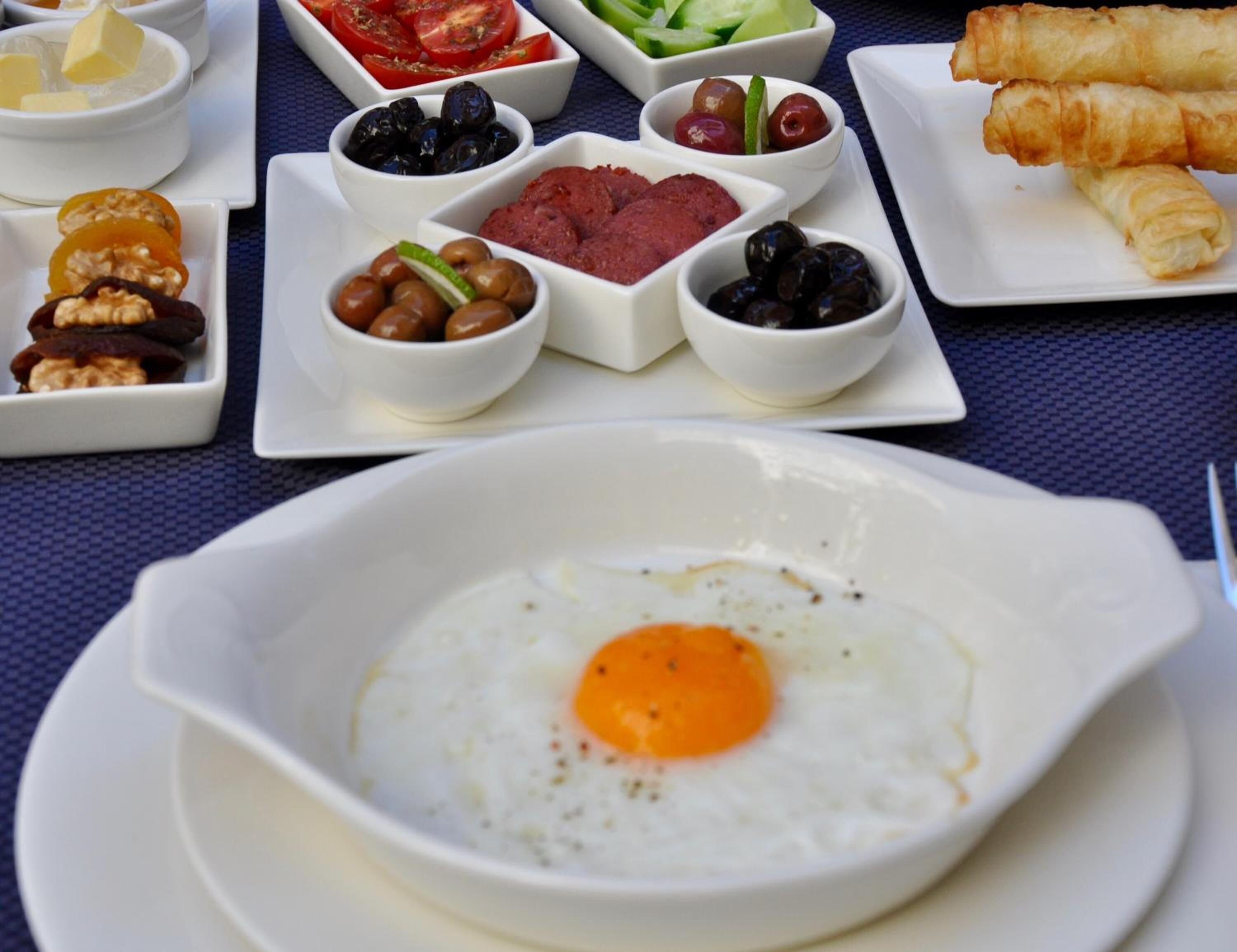 Un assortiment de plats variés pour le petit-déjeuner, comprenant des œufs, des olives, des tomates et des viennoiseries.