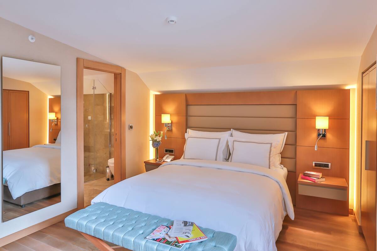 A hotel room with a large bed, bedside tables, a mirror, a shower, and a wooden headboard.