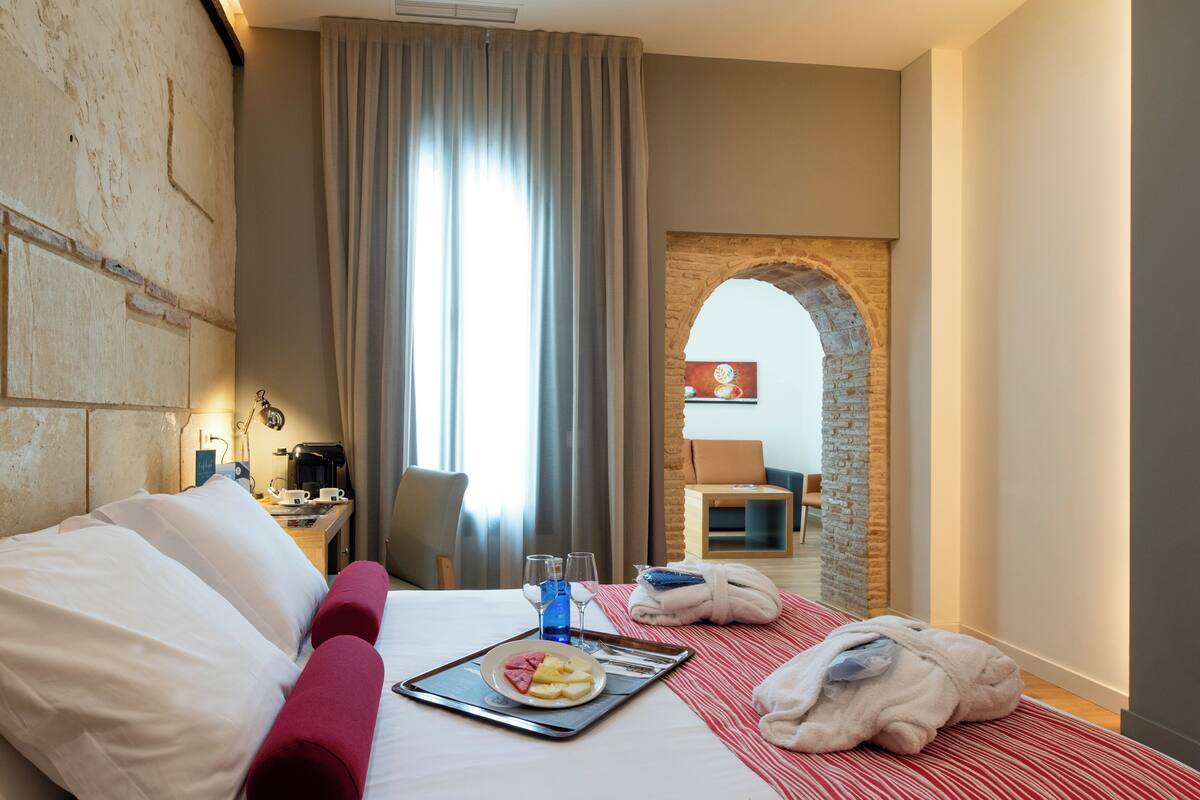 Hotelkamer met een bed, een dienblad met ontbijtartikelen, een koffieapparaat en uitzicht door een boogvormige deuropening.
