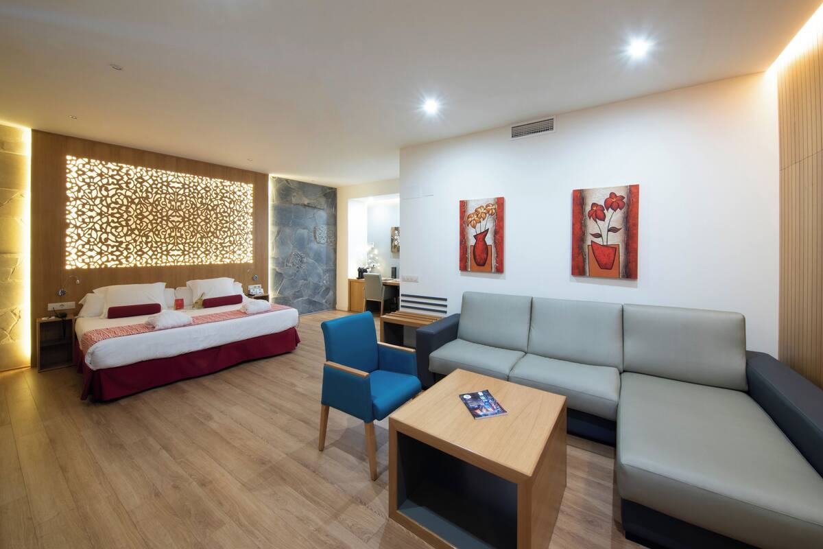 Een moderne hotelkamer met een bed, een blauwe stoel, een grijze bank en twee schilderijen aan de muur.
