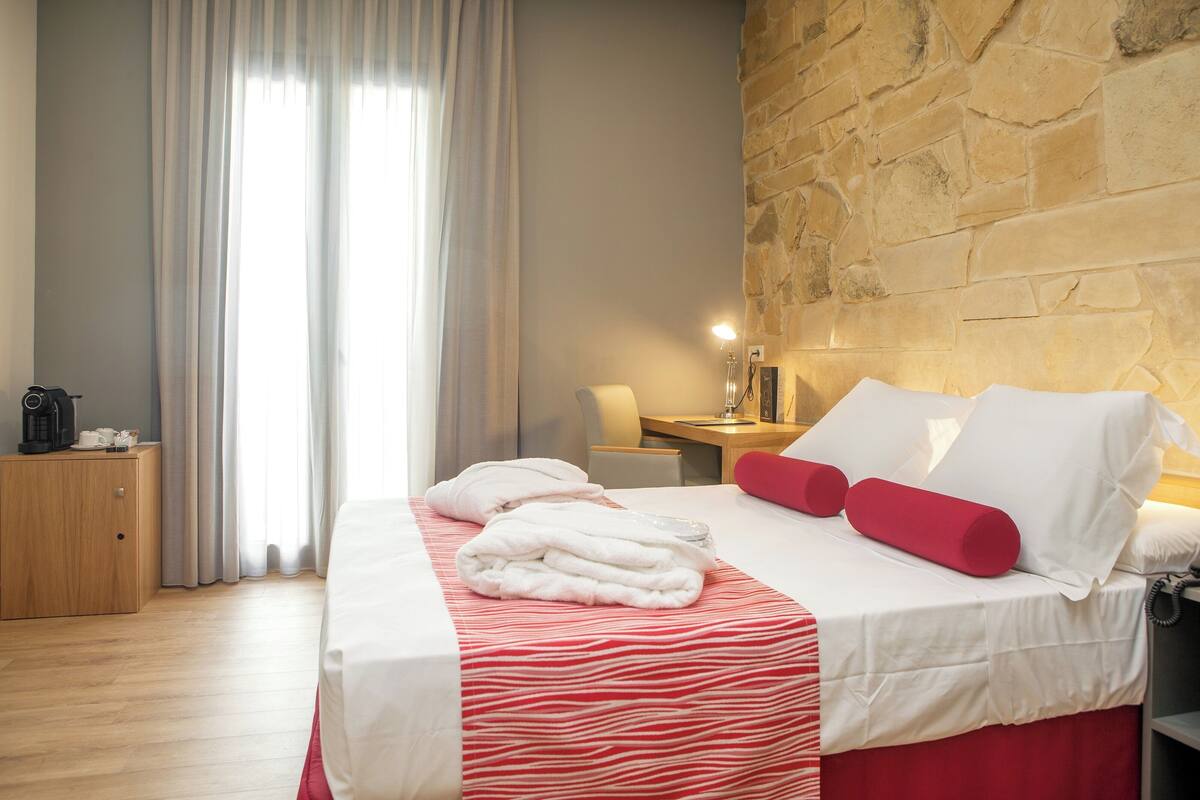 Een hotelkamer met een bed, een houten bureau, een lamp en een stenen muur.