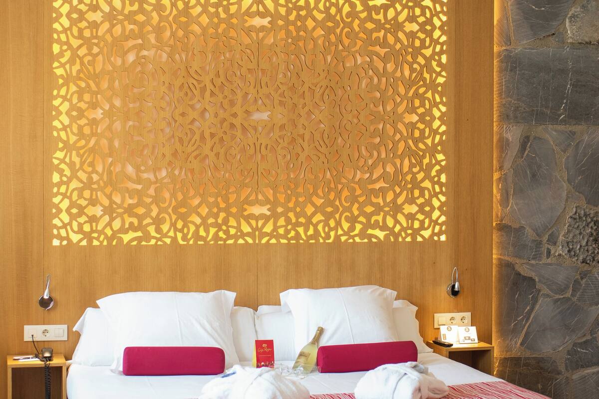 Een hotelkamer met een groot bed, houten lambrisering, een accentmuur van steen en een decoratief scherm.