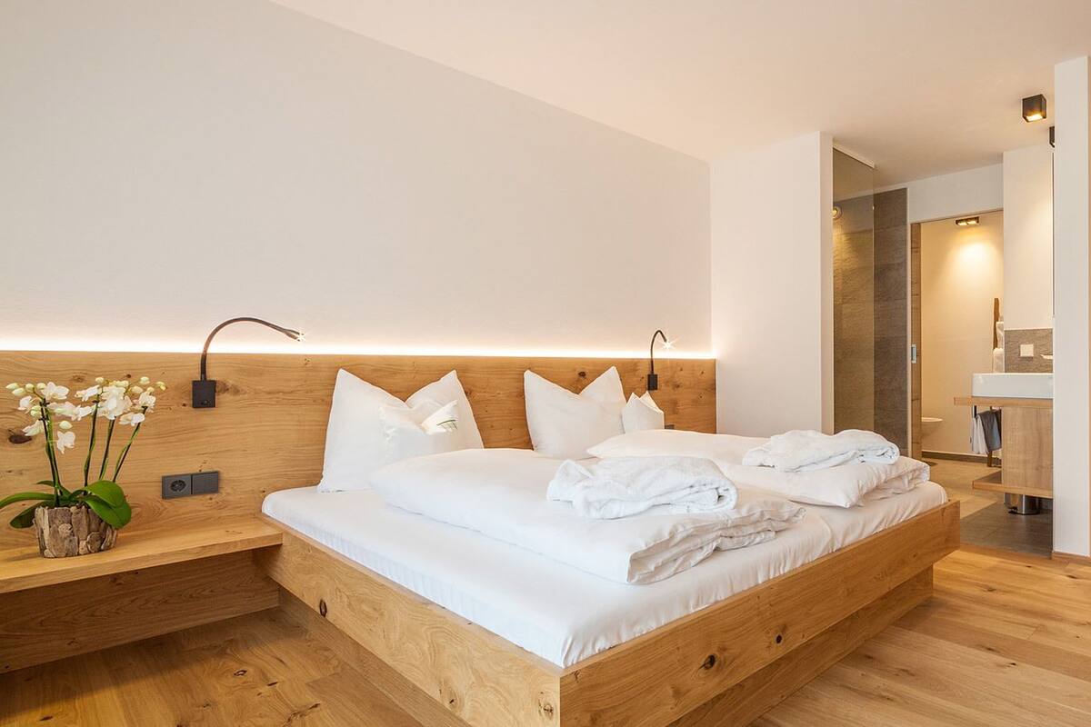 A modern hotel room with a wooden bed, white linens, a bedside plant, and a wooden nightstand.