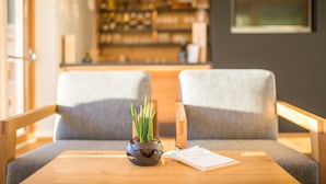 Un interior moderno con dos sillones grises tapizados, una mesa de madera con planta en maceta, y una zona de bar al fondo.