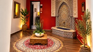 A hallway with a red wall, a patterned wall decoration, a wooden bench, and a potted plant. - Hotel Tafoukt (Marrakech)