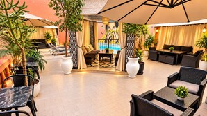 An outdoor seating area with tables and chairs, surrounded by potted plants and a pool in the background. - Hotel Tafoukt (Marrakech)