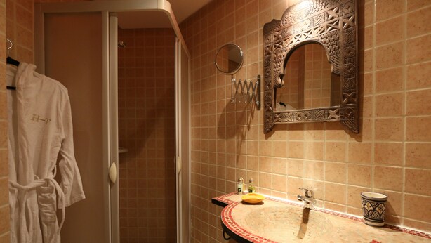 A bathroom with a tiled wall, a sink with a decorative mirror, and a robe hanging on a rack. - Hotel Tafoukt (Marrakech)