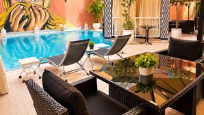 A poolside area with wicker furniture, a glass table, and a mural. - Hotel Tafoukt (Marrakech)