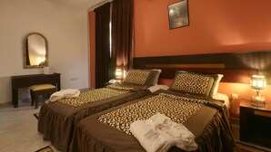 A hotel room with two beds, a desk, a mirror, and a nightstand with a lamp. - Hotel Tafoukt (Marrakech)