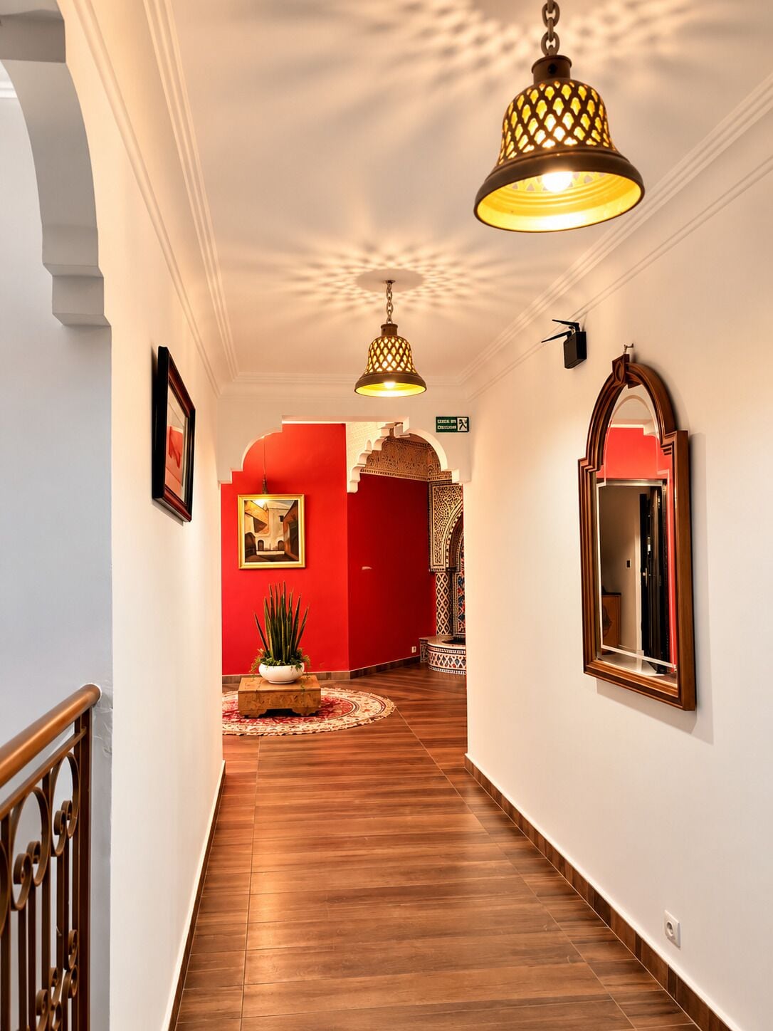 Un pasillo con suelo de madera, pared roja y una lámpara colgante.