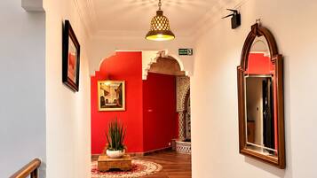 Un pasillo con suelo de madera, pared roja y una lámpara colgante.