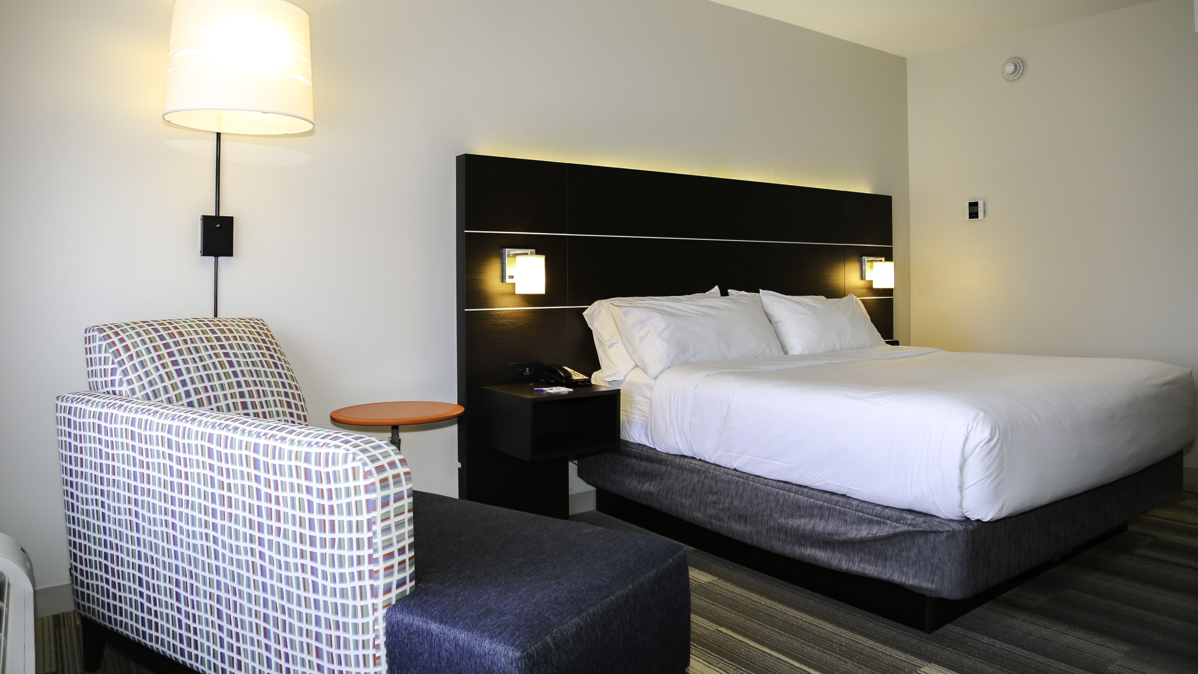 Una camera d'albergo con un letto, una sedia, un tavolino e una lampada.