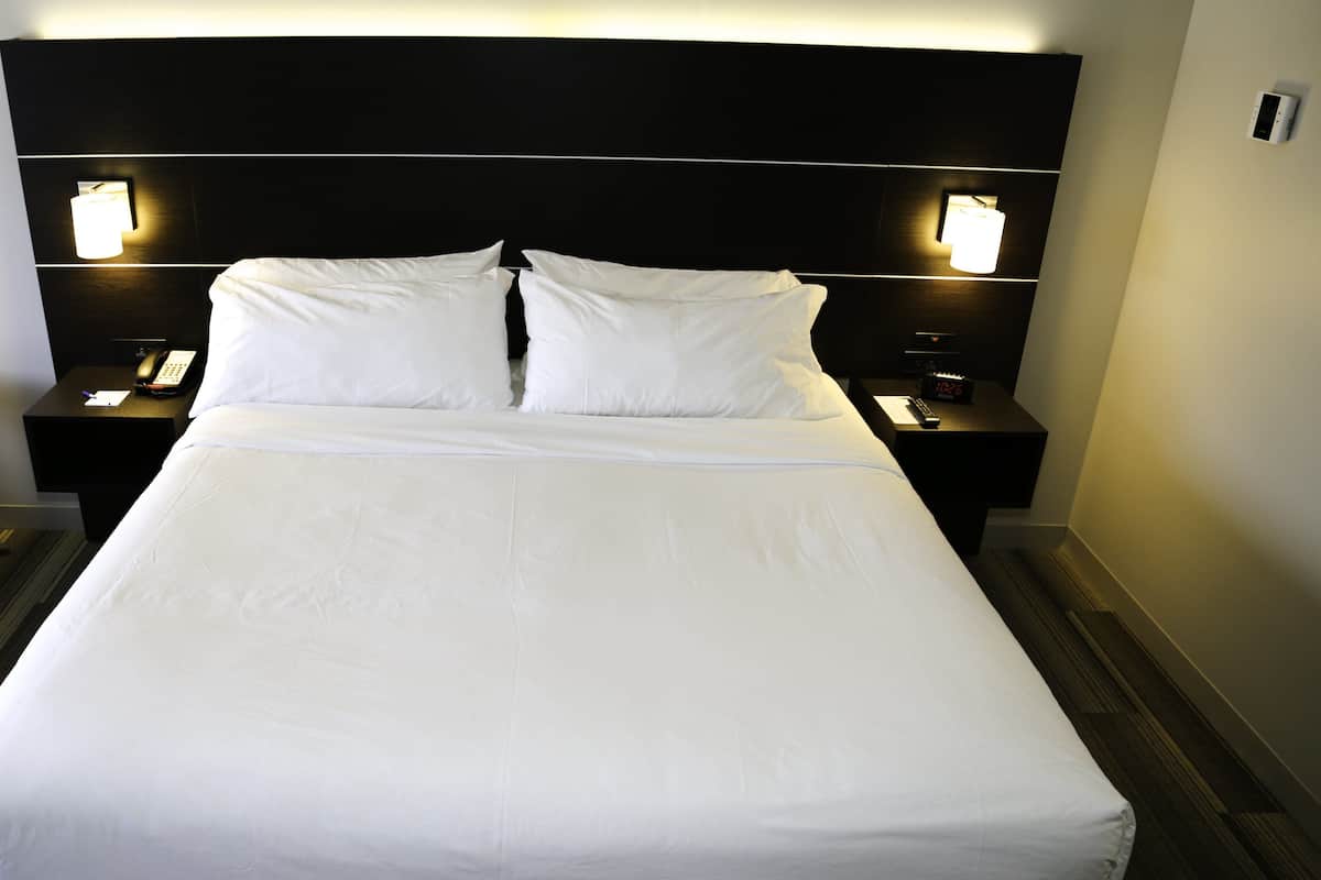 Una habitación de hotel con una cama grande, dos mesitas de noche, un teléfono y una lámpara fijada a la pared.
