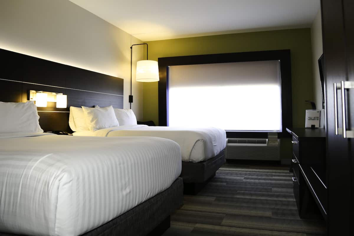 Habitación de hotel con dos camas, un ventanal grande, aire acondicionado instalado en la pared y un armario de madera oscura.