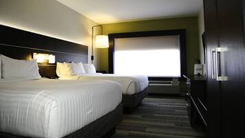 Habitación de hotel con dos camas, un ventanal grande, aire acondicionado instalado en la pared y un armario de madera oscura.