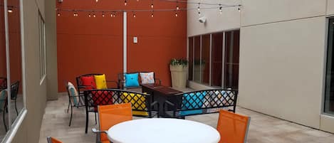 An outdoor patio with a round table and orange chairs, a black metal fence, and string lights.