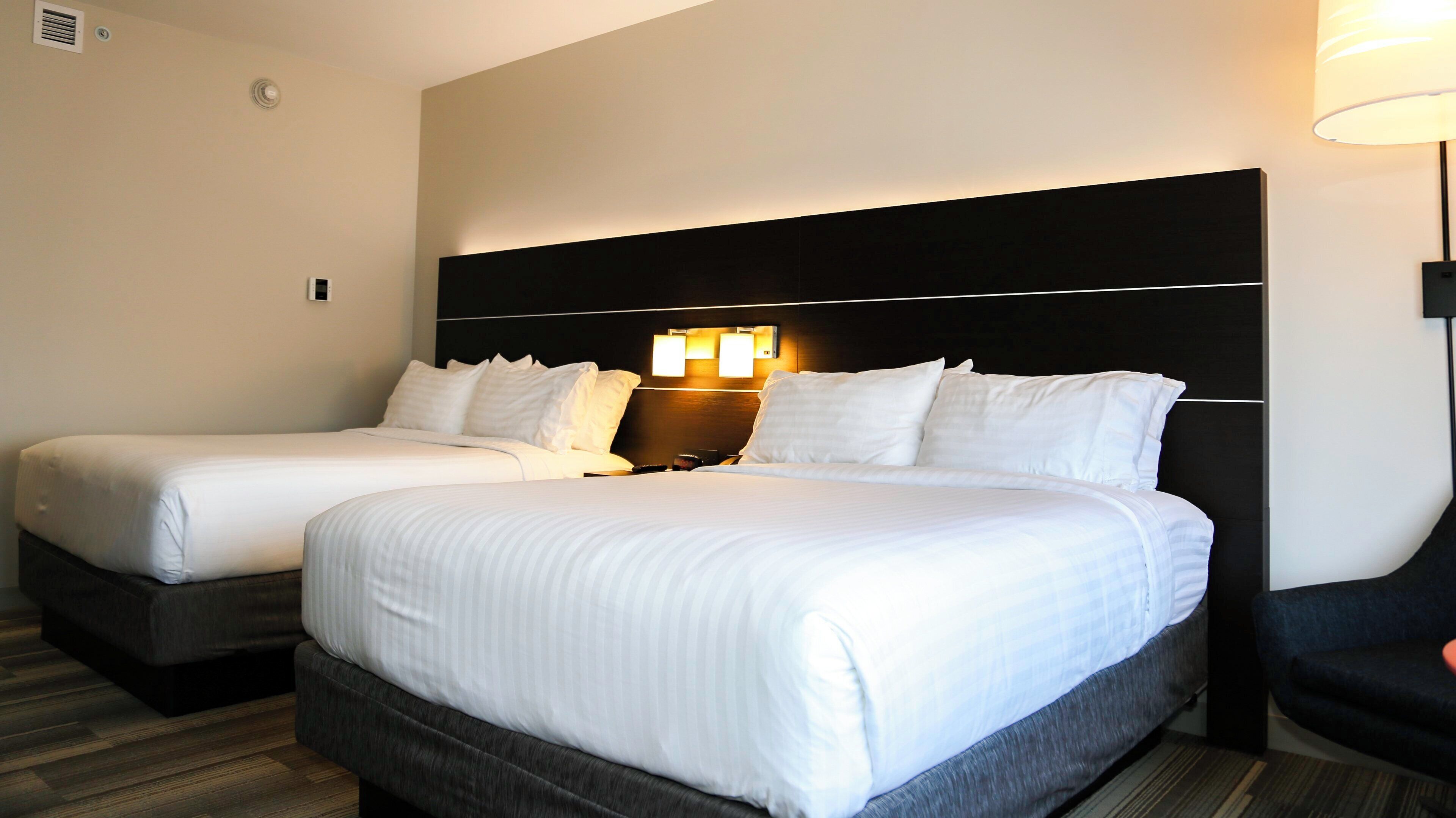 Ein Hotelzimmer mit zwei Betten, einem dunklen Kopfteil und einer Wandleuchte.
