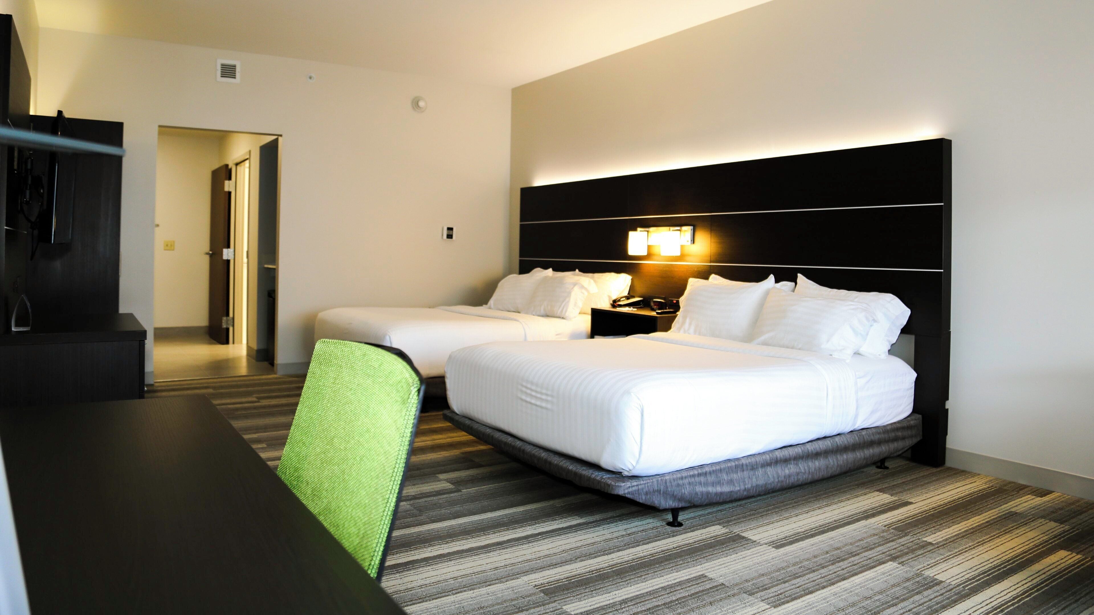 Une chambre d’hôtel avec deux lits, un bureau, une chaise et une table de chevet avec une lampe.