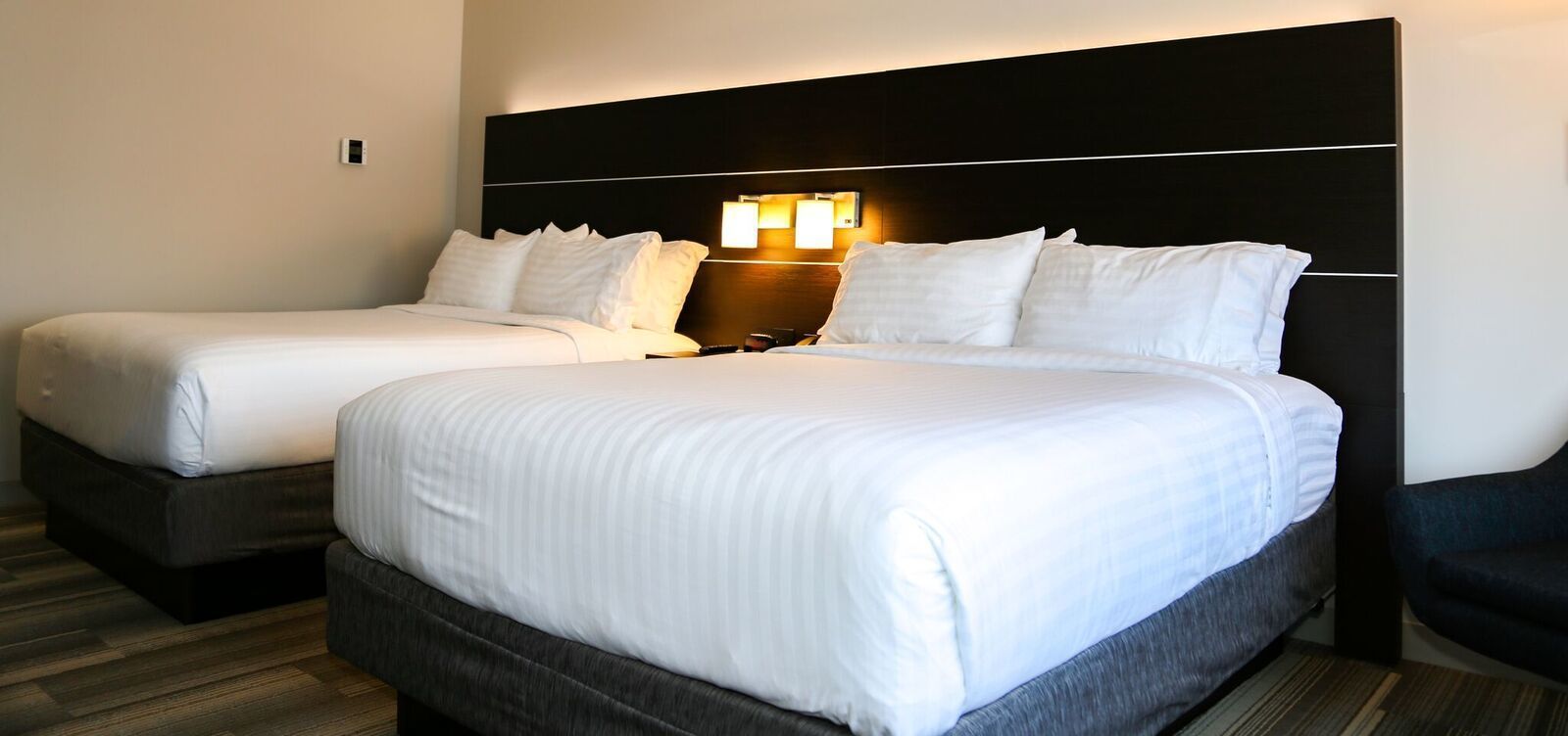A hotel room with two beds, a dark headboard, and a wall-mounted light fixture.