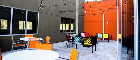 An outdoor patio with tables and chairs, string lights, and a glass wall.