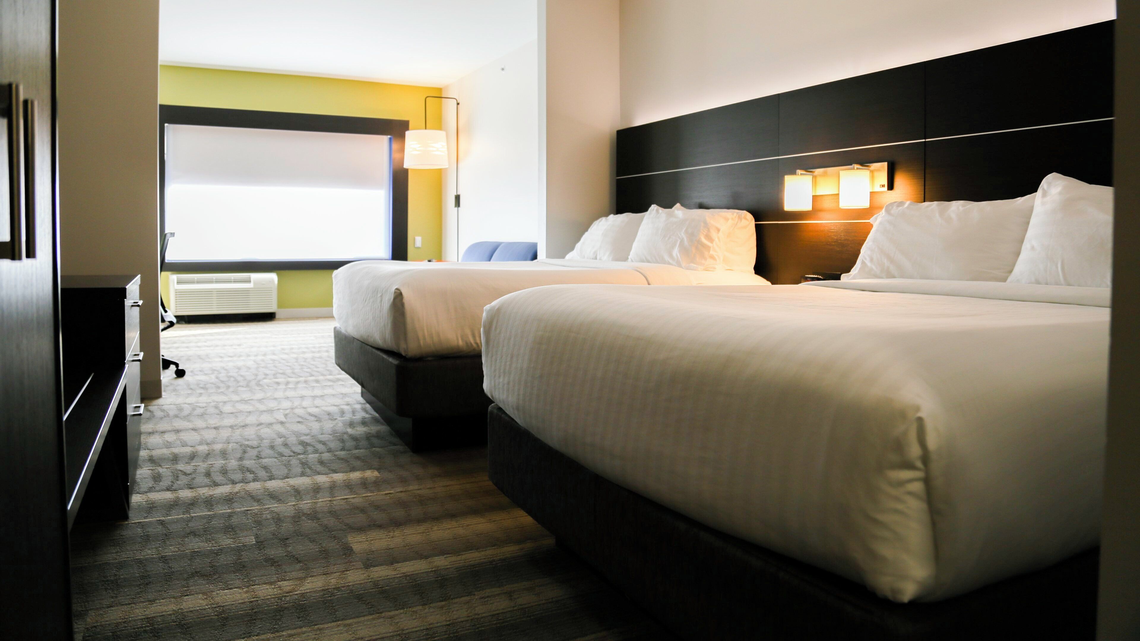 A hotel room with two beds, a desk, and a large window.
